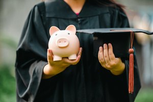 A female student wearing a black cloak and holding a piggybank and a hat
