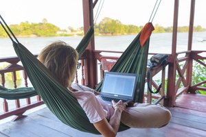 A young woman working in her laptop while laying on a hammock
